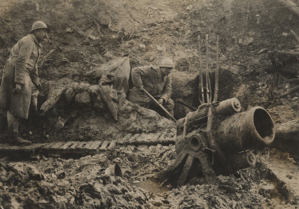 Photographie sephia de deux soldats dans une tranchée boueuse utilisant un canon de tranchée court et trapu.