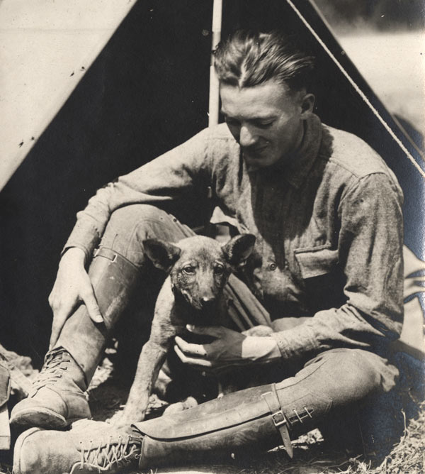 Photographie en noir et blanc d'un homme blanc assis en uniforme de combat militaire avec un petit chien sur ses genoux.