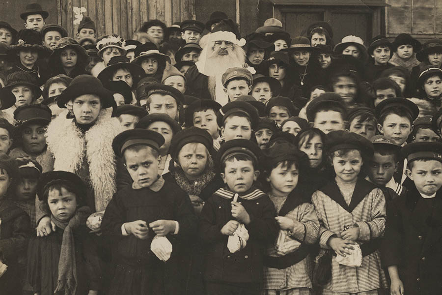 Black and white photograph of a large crowd of children with a man dressed as Santa Claus in the middle.