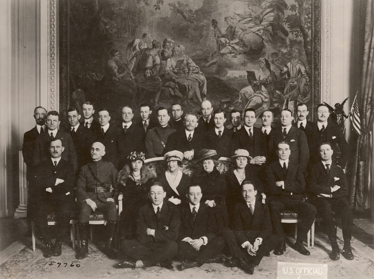 Black and white photograph of a group of men and women in suits and suit dresses posing under a large painting