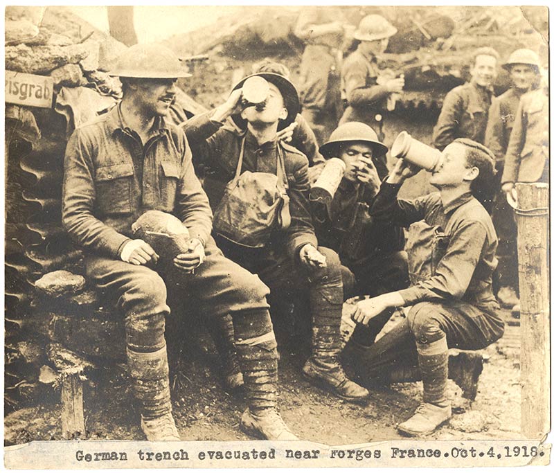 Sepia photograph of a group of WWI-era soldiers sitting in a trench with mugs of beer.