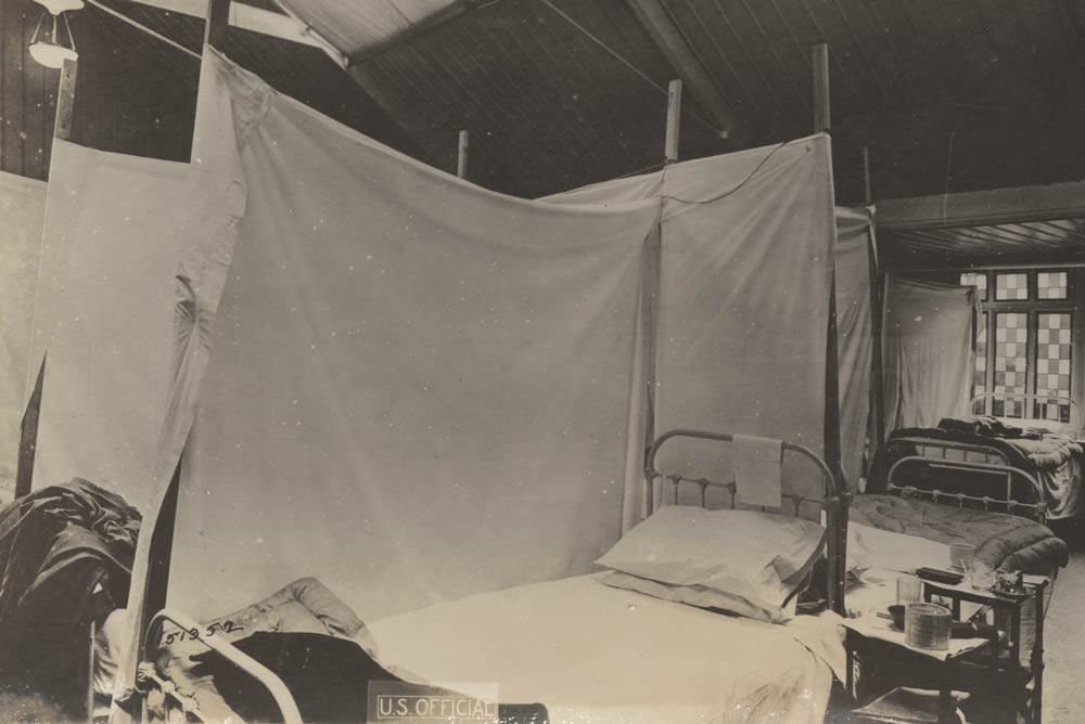 Black and white photograph of rows of hospital beds with white sheets strung up between beds.