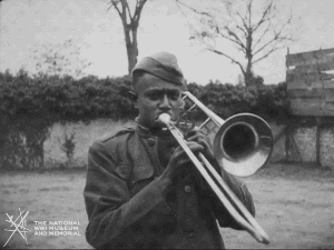 Animated gif of black and white film footage. A Black man in military uniform plays a trombone.