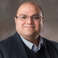 Headshot of a larger light-skinned bald man wearing frameless glasses