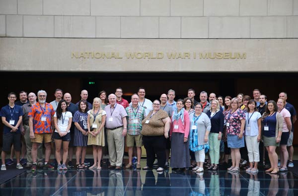 Modern photograph of a large group of adults posing for a picture on the glass bridge inside the Museum.