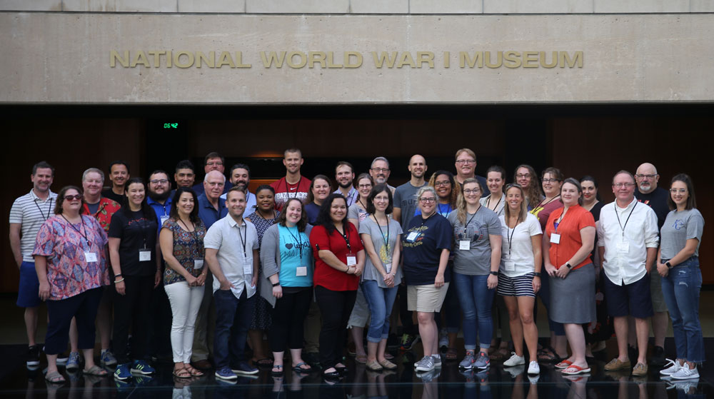 Modern photograph of a large group of adults posing for a picture on the glass bridge of the Museum.