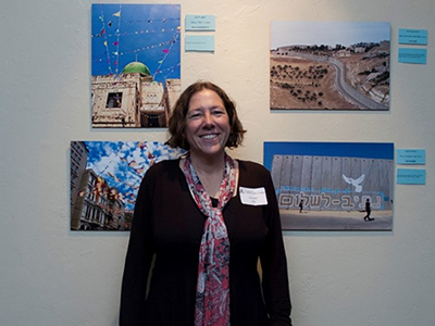 Photograph of a middle-aged white woman with a dark brown bob standing in front of a wall of photographs