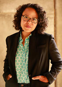 Headshot of a darker-tanned woman with a curly bob and glasses