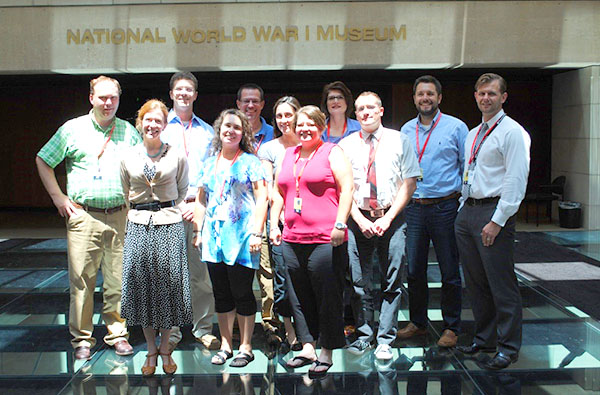 Modern photograph of a small group of adults posing for a picture on the glass bridge inside the Museum on a very sunny day.
