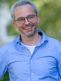 Headshot of a light-skinned middle-aged white man with silvering hair and beard wearing glasses