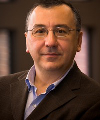 Headshot of a middle-aged light-skinned man wearing round thin-framed glasses