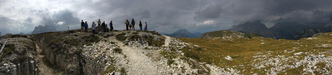 Panoramic shot of a trench stretching away to the left. In the distance small humans are silhouetted against the cloudy sky.