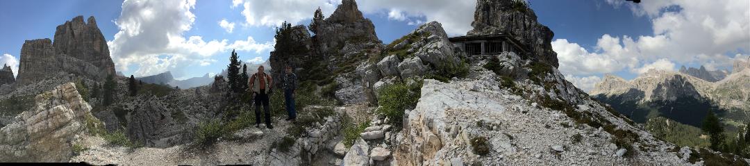 Panoramic shot of mountain peaks and valleys. Two tour members pose in the foreground.