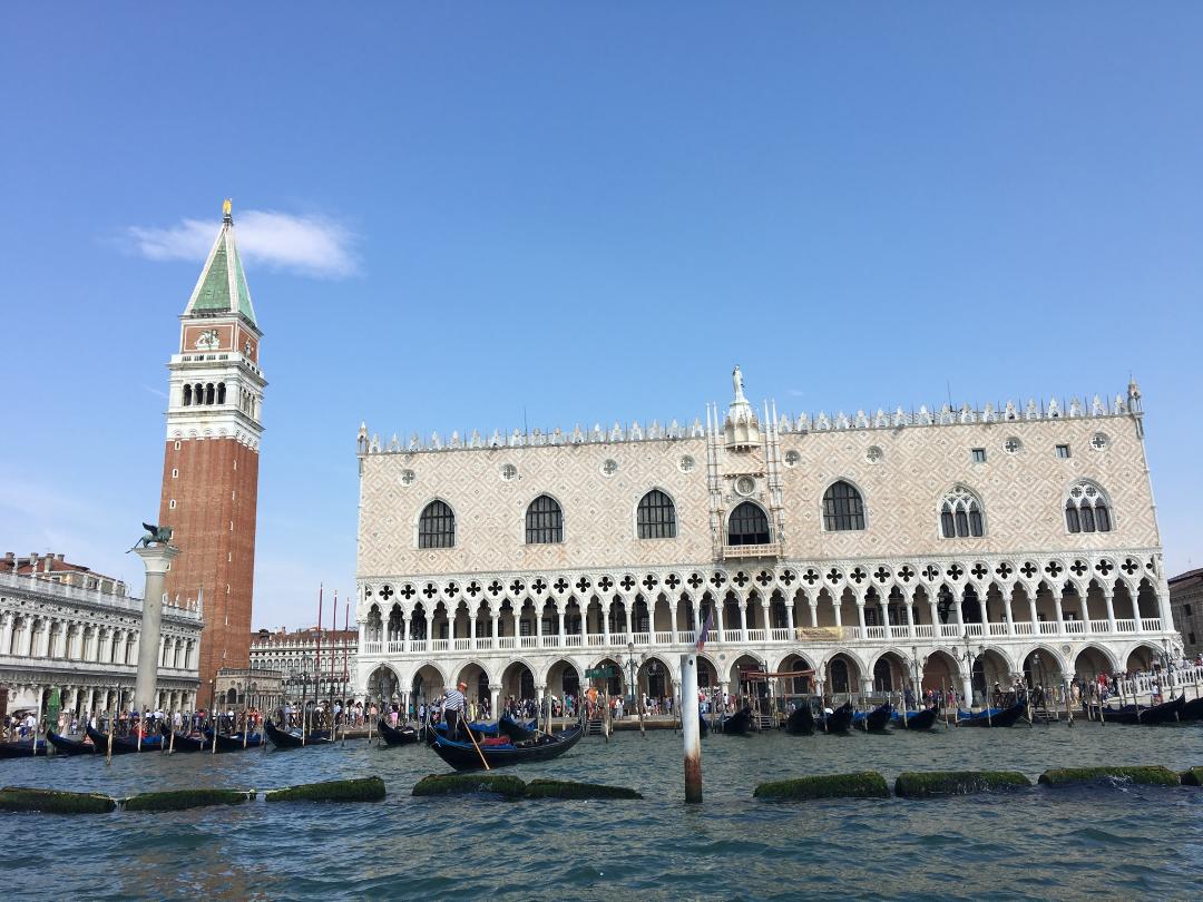 View of a Venice canal with a gondola poling through it and a medieval building on the far side.