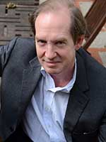 Headshot of a white man with thinning brown hair wearing a dark grey suit jacket