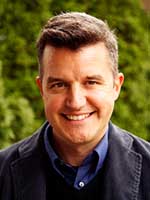 Headshot of a white man with short brown hair wearing a black canvas jacket