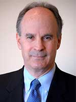 Headshot of a middle-aged balding white man with grey hair and mustache wearing a black suit jacket