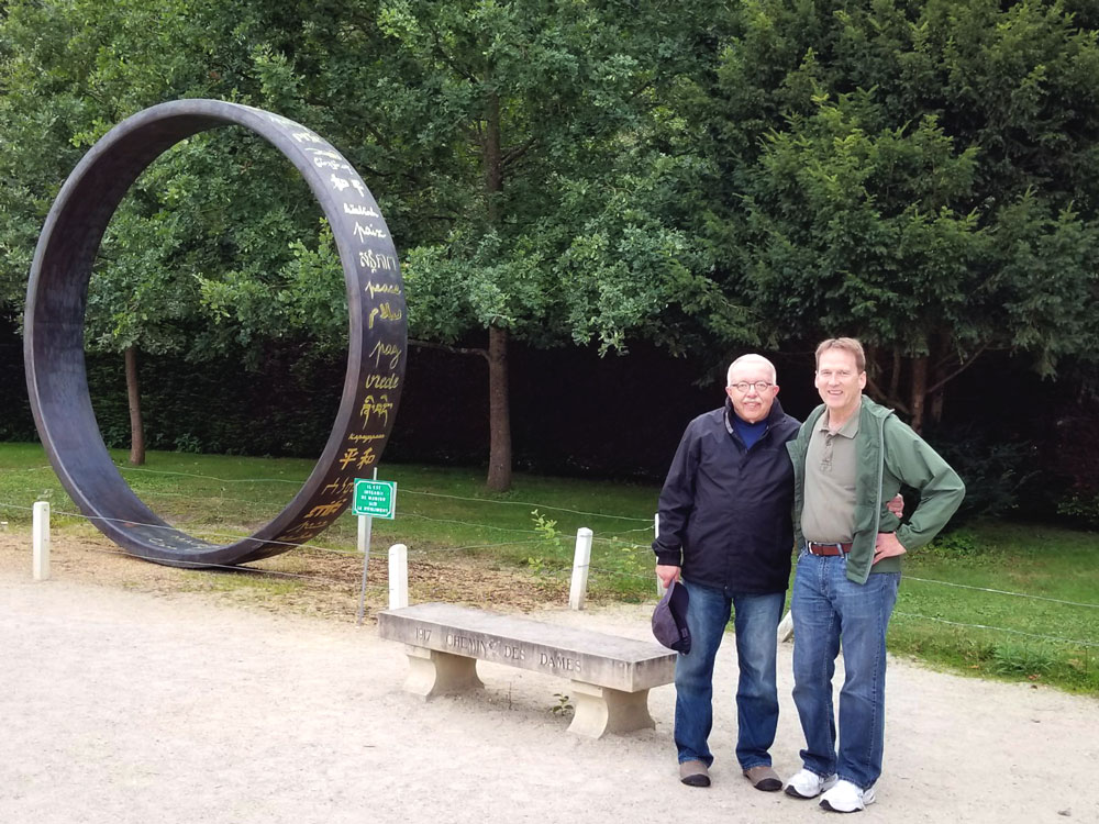 Two men posing near a memorial shaped like an upright ring.