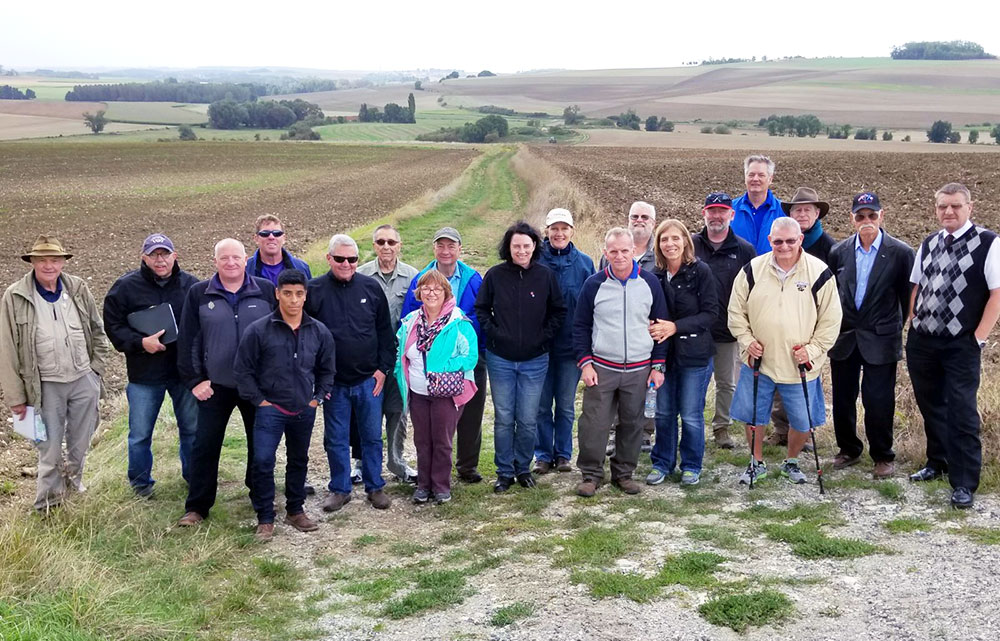 The tour group poses in front of a grassy field.