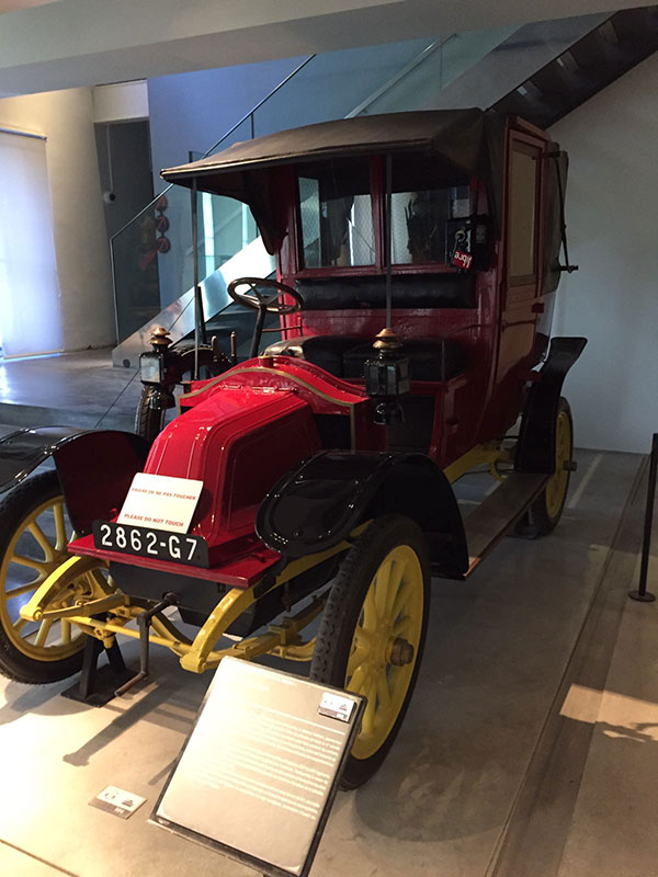 Photograph of a museum display of a WWI-era red automobile with yellow wheels.