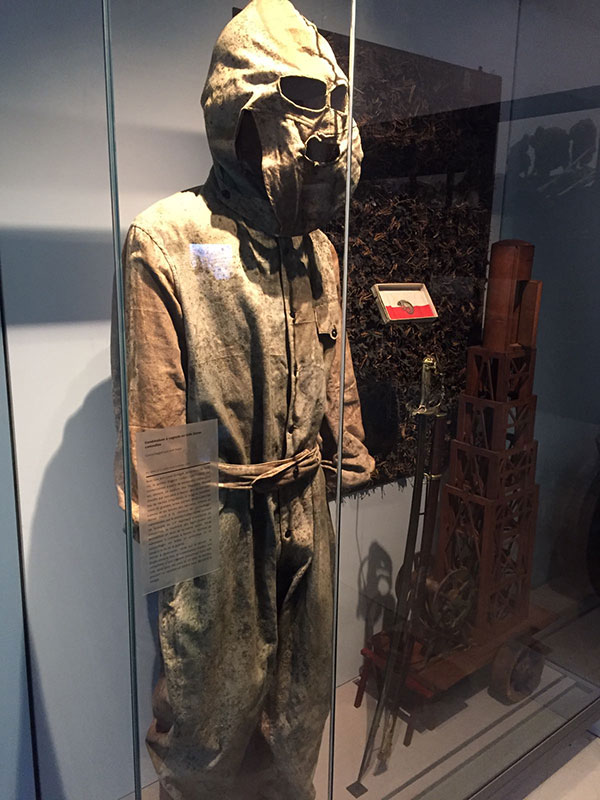 Photograph of a museum display of a brown-colored camouflage suit with gas mask.