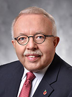 Headshot of an older white man with grey hair wearing glasses and a black suit jacket