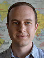 Headshot of a white man with brown hair wearing a blue striped button-down shirt