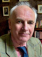 Headshot of a balding white man with white hair wearing a green suit jacket