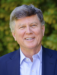 Headshot of an old white man with grey hair wearing a blue suit jacket