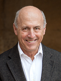 Headshot of an old balding white man in a dark grey suit jacket