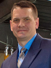 Headshot of a white man with close-cropped brown hair in a blue suit jacket.