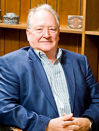 Headshot of an older white man with white hair in a blue suit jacket.