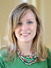 Headshot of a white woman with long blonde hair in a green shirt and colorful beaded necklace.