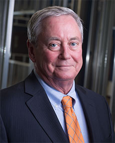 Portrait of an older white man with silver hair wearing a black suit jacket