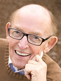 Portrait photograph of an old bald white man wearing glasses and a camel sweater