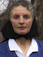Headshot of an older white woman with grey hair wearing a black head scarf and a blue shirt.