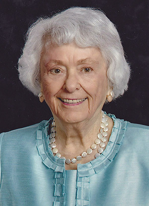 Portrait photograph of a smiling elderly white women with silver hair wearing a light blue shirt.