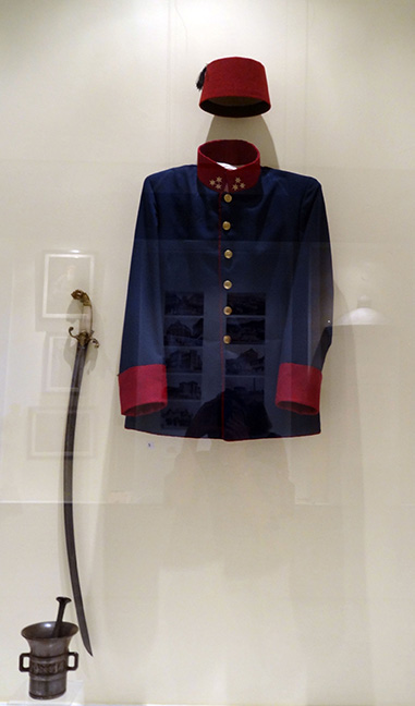Display of a blue uniform jacket, red cap, and curved sword