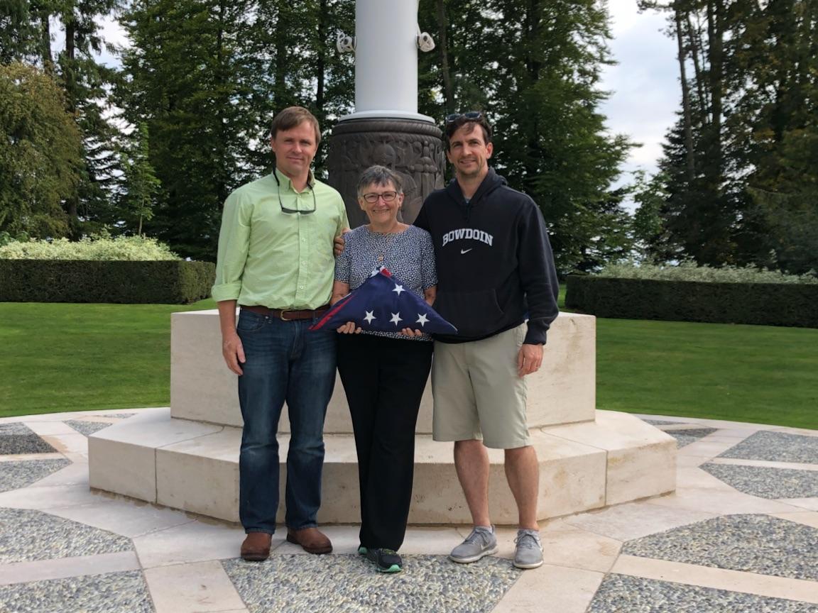 A man, a woman, and a man posing in front of a flag pole. The woman in the center is holding a U.S. flag folded into a triangle.