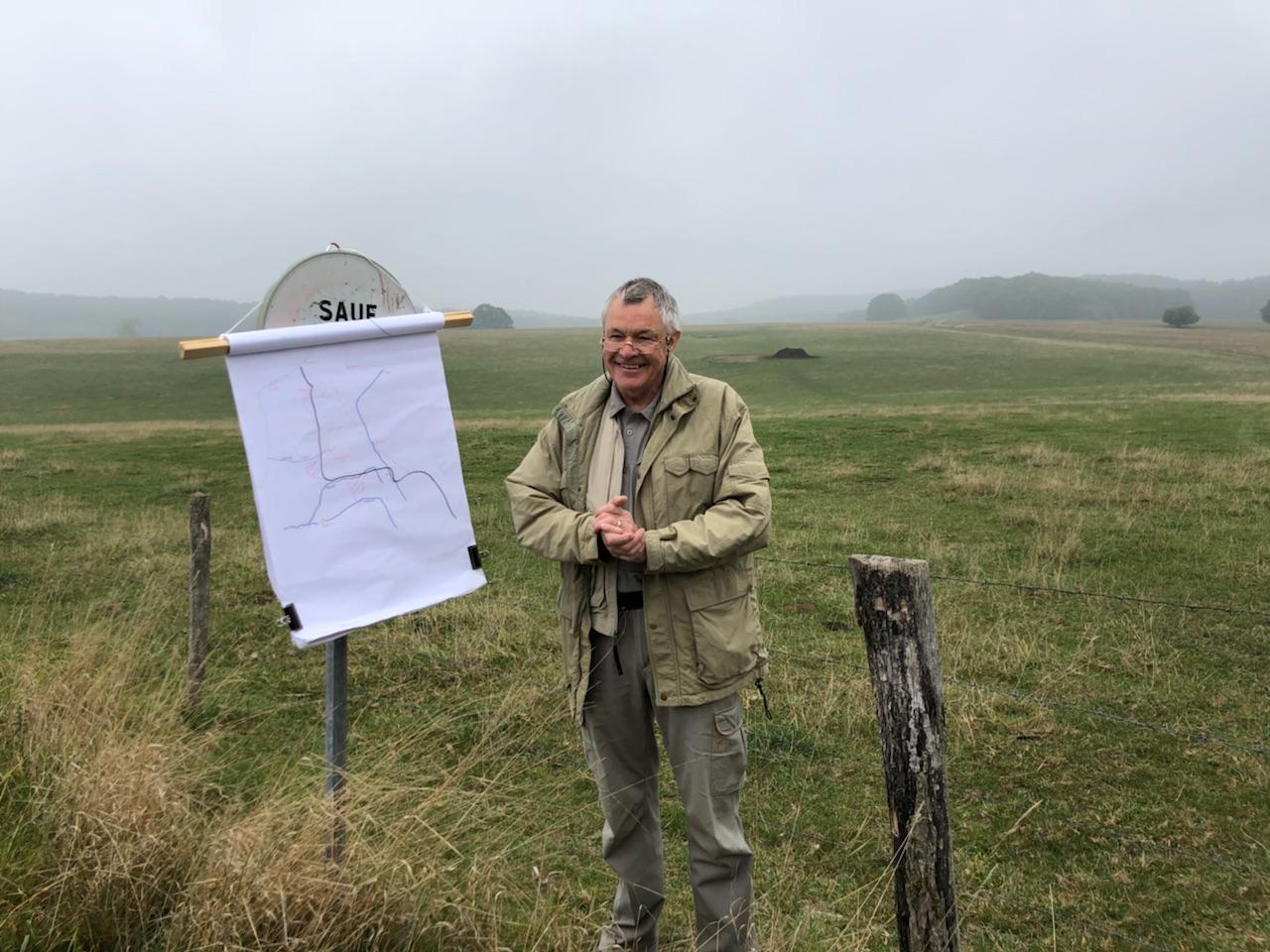 A man standing in a grassy field with an easel showing a map.