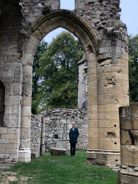 A person dressed in black stands just beyond the archway of a destroyed building.