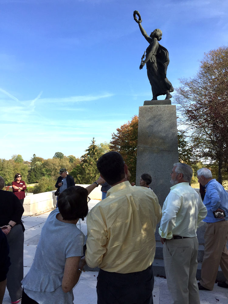 Tour group gathered around a bronze statue of a woman in robes with her arm raised