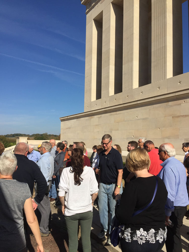 Tour group milling about near a columned memorial