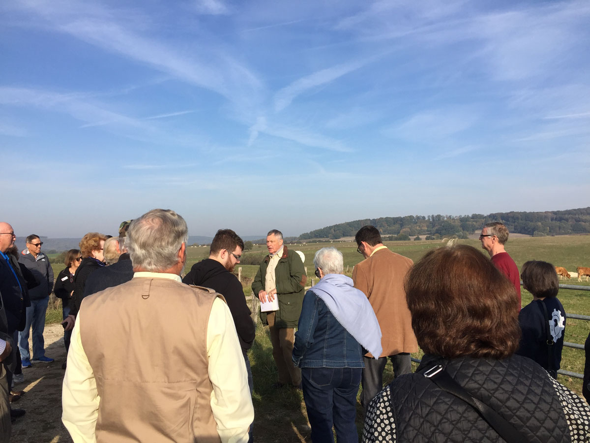 Tour group gathered around the tour guide next to a field.