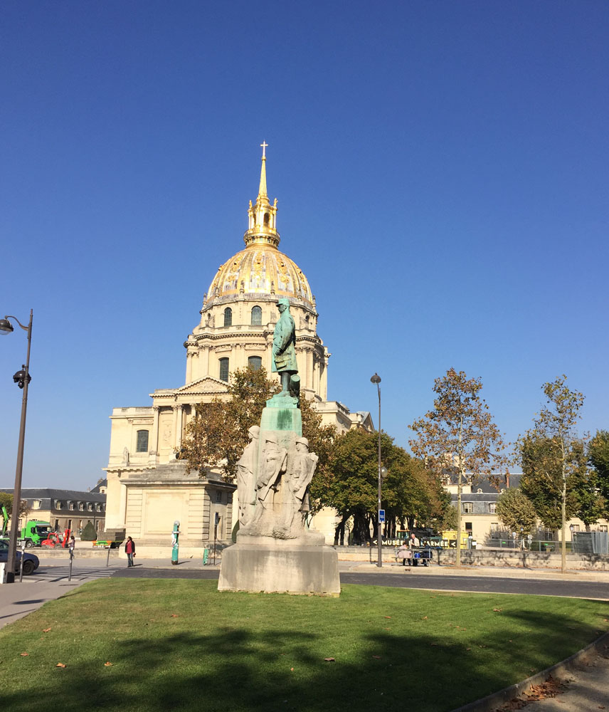 Building with a rotunda. A copper statue on a plinth in front of it.