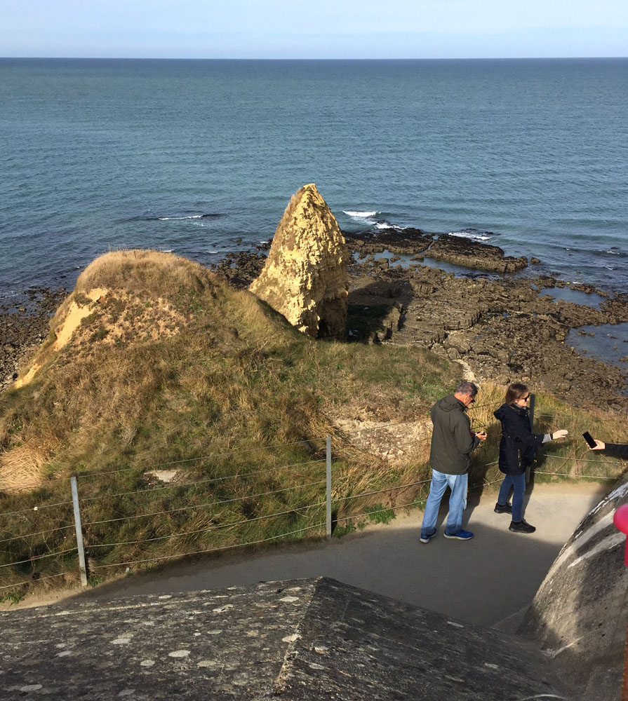 A spit of land extending into the ocean with a very tall boulder on it.