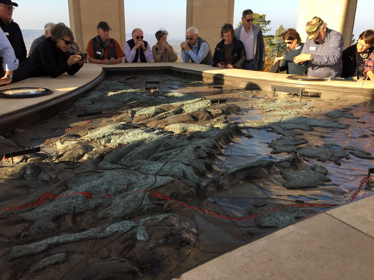 Tour group gathered around a 3D topographical map of a battlefield