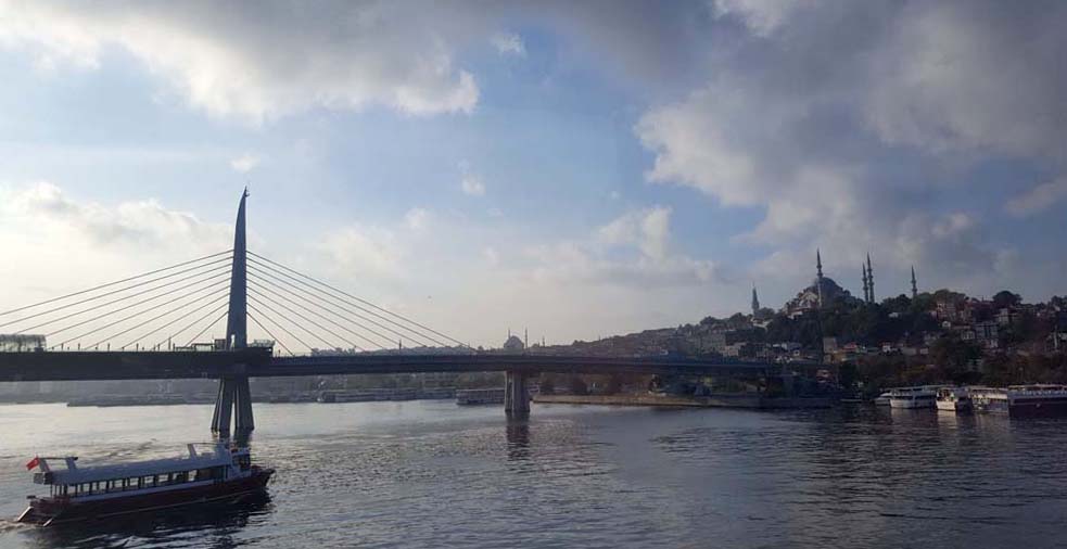 View of a modern suspension bridge across a body of water with a mosque on the opposite shore