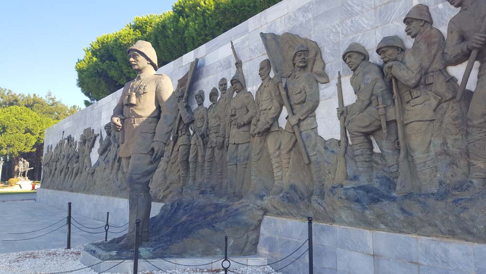 Statue of a soldier in front of a wall with lots of figures carved in bas-relief