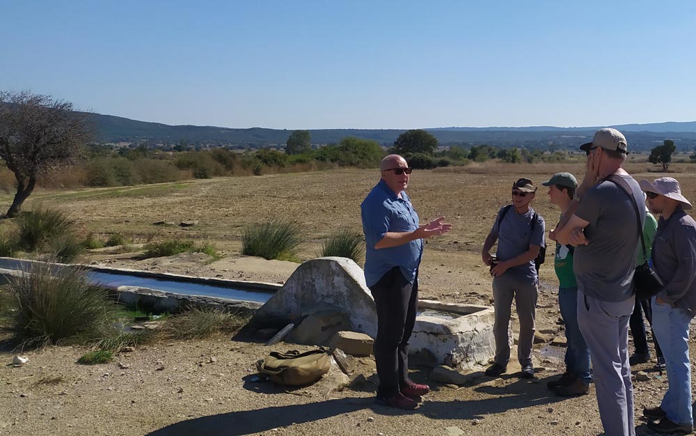 A tour guide explaining something to a group of people standing in a sun-blasted field